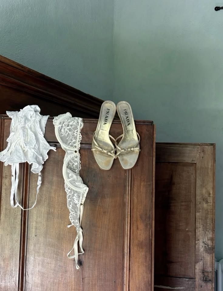 Lace lingerie and gold sandals draped over an old wooden wardrobe