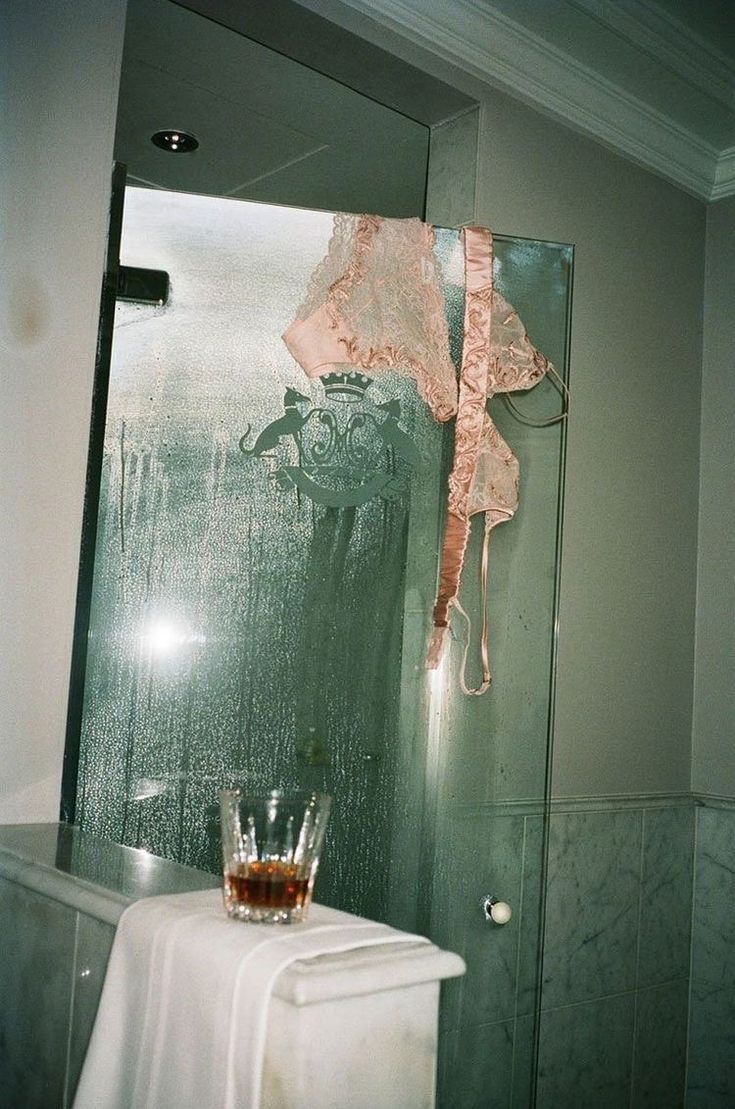 A steamy glass shower with pink lingerie hanging on the door