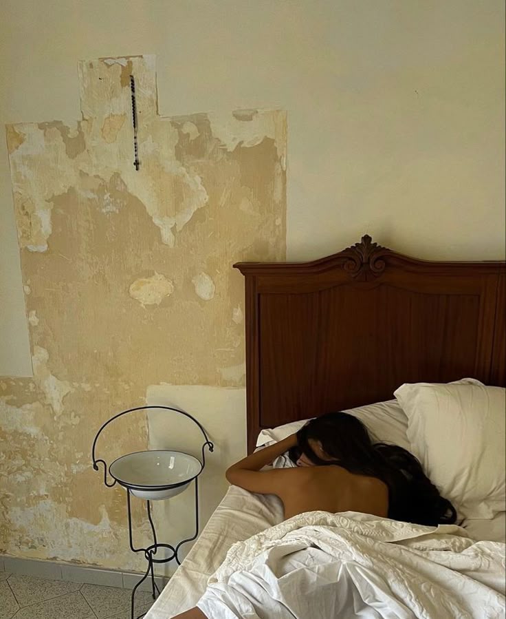 A woman asleep in a bed against a worn plaster wall